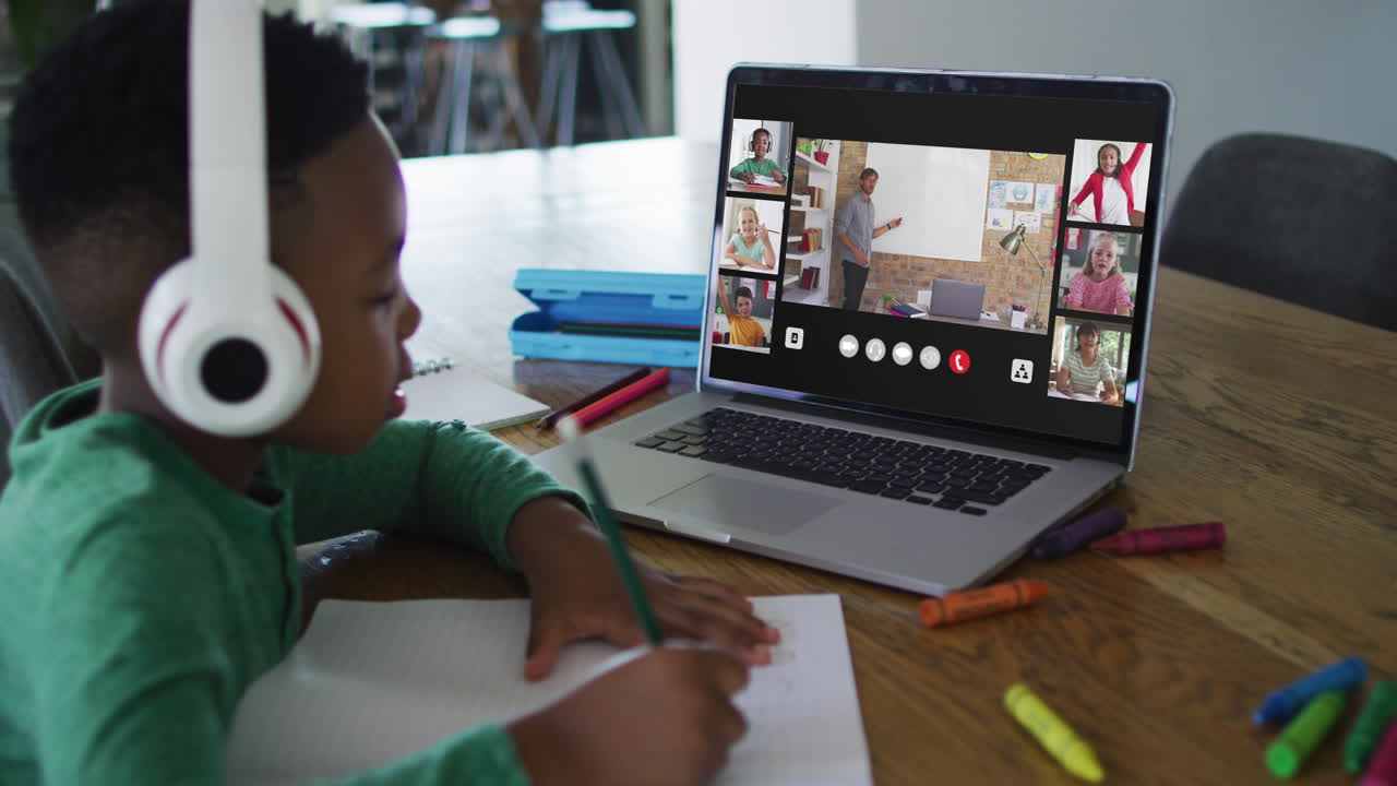 Schoolboy using laptop for online lesson at home, with diverse teacher and class on screen