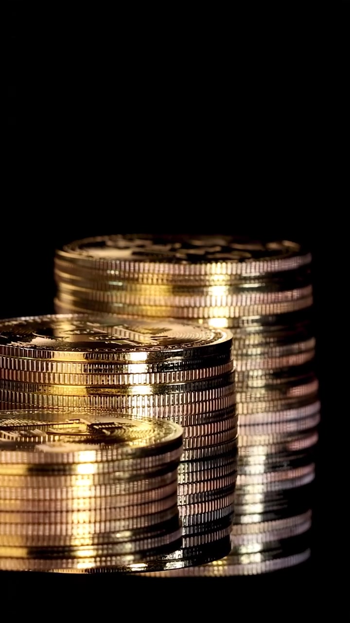 Stacks of gold digital tokens rotate smoothly under dramatic lighting, close-up, black background