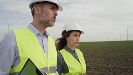 two caucasian engineers walking on wind turbine field and discussing.