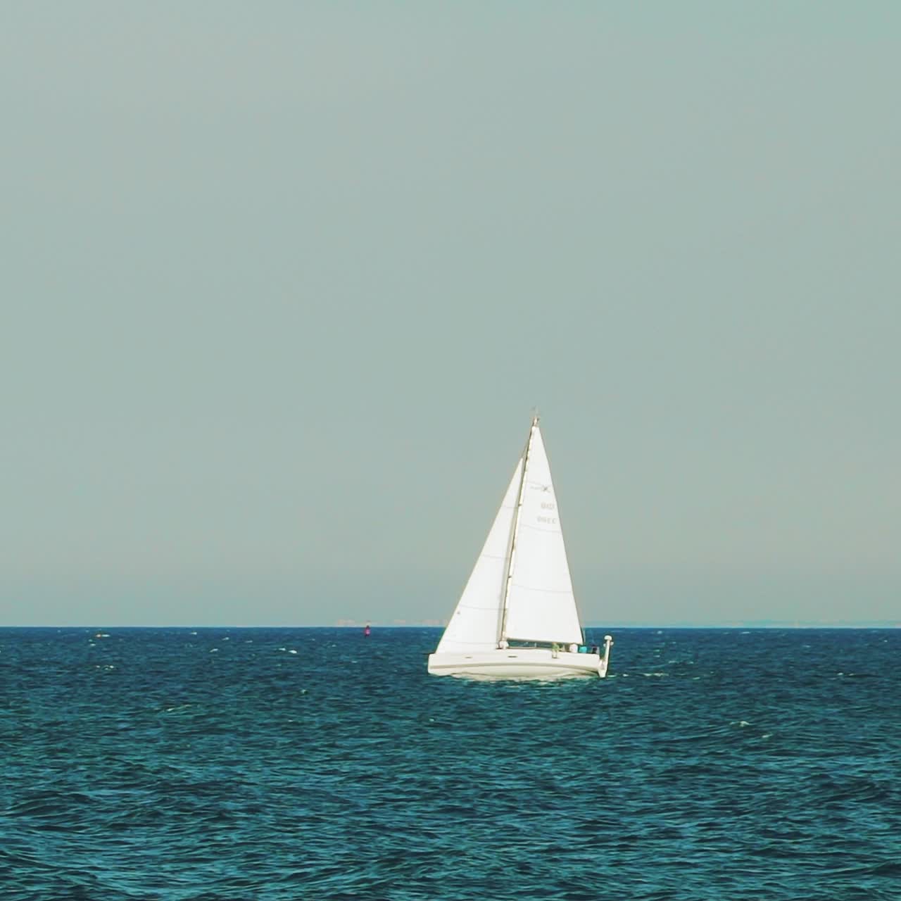 white sailboat is sailing on the sea far from the coast in the summer. Slow motion