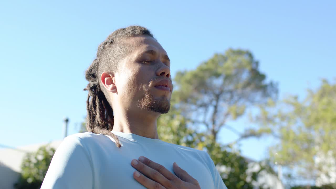 Homem afro-americano colocando a mão esquerda no peito, respirando, centralizando-se no jardim com smartwatch