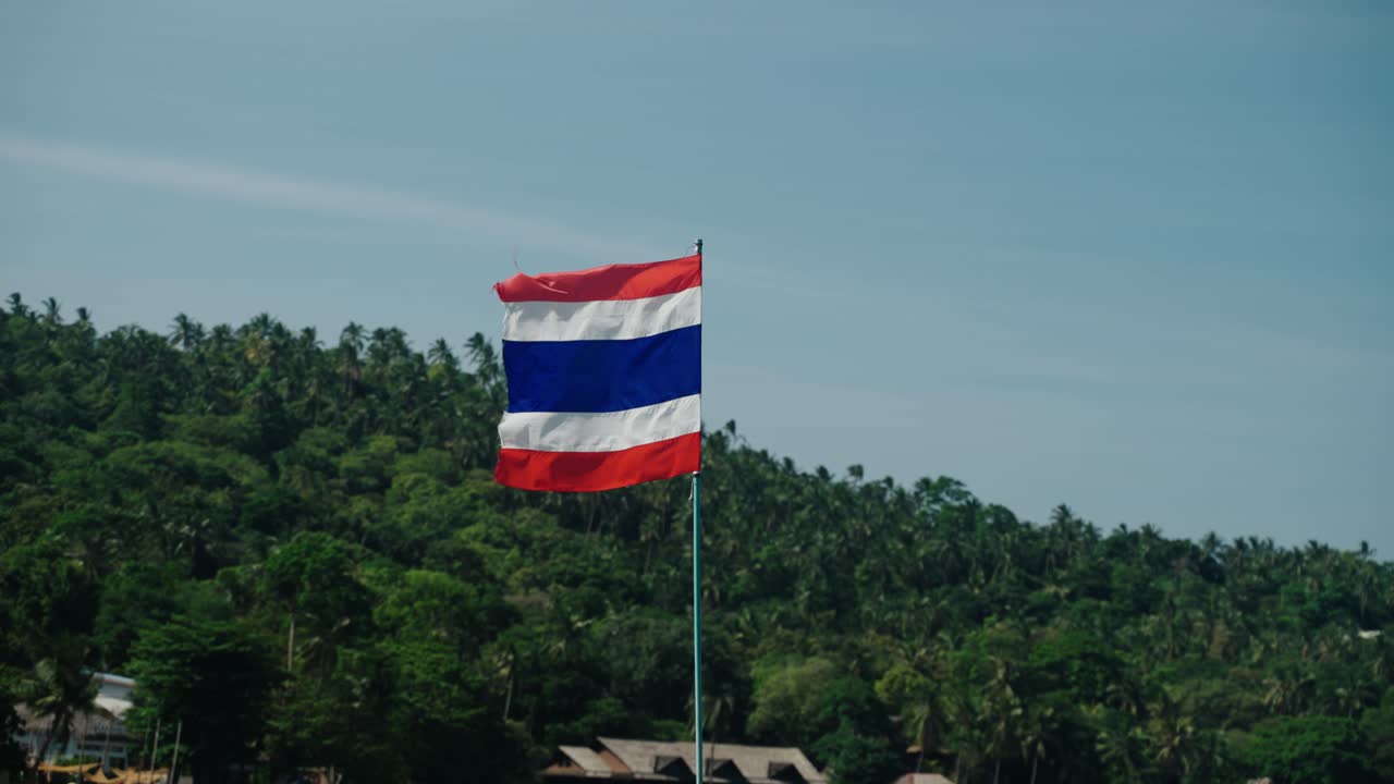 Thai national flag waves in Ko Tao, Thailand, above green hills and palm trees