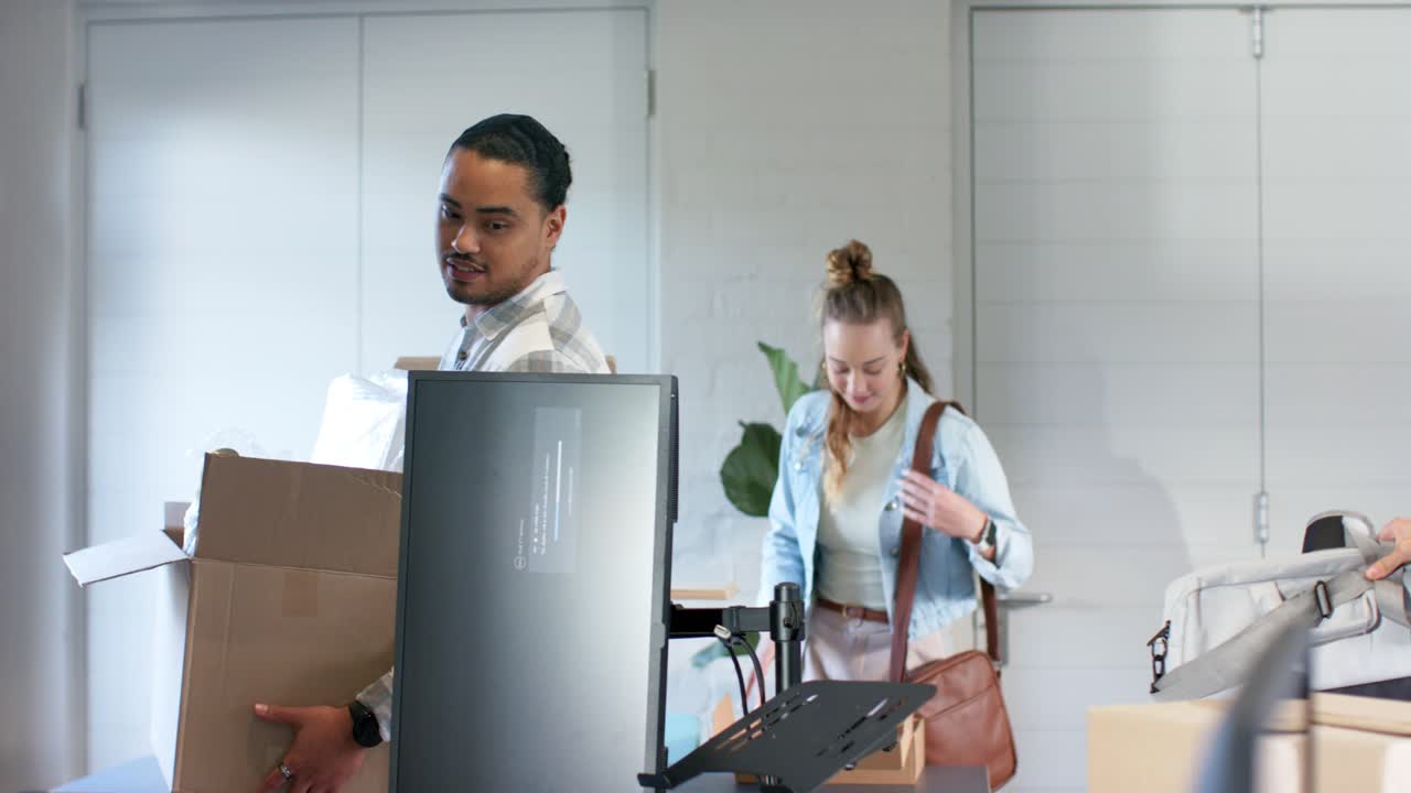 Diverse team entering office carrying boxes unpacking monitor arranging desk for setup, copy space