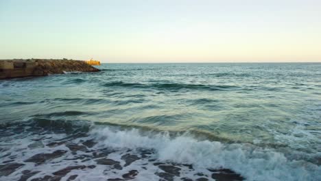 Wellen-Brechen-Sanft-Am-Strand-Von-Costa-Garraf-Mit-Einem-Fernblick-Auf-Eine-Zementfabrik-In-Barcelona