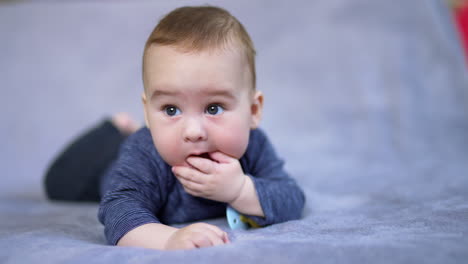 healthy adorable kid lies on bed shoving his fingers into a mouth. close up portrait of a beautiful baby lying peacefully on bed.