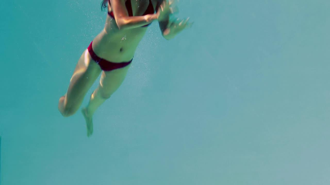 Bella bruna che si tuffa in piscina e saluta