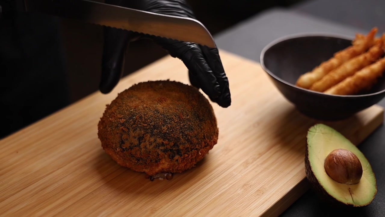 Chef coupant une grande croquette frite sur une planche en bois