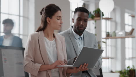young team leader woman brainstorming with businessman colleague using laptop computer showing ideas pointing at screen working together in office