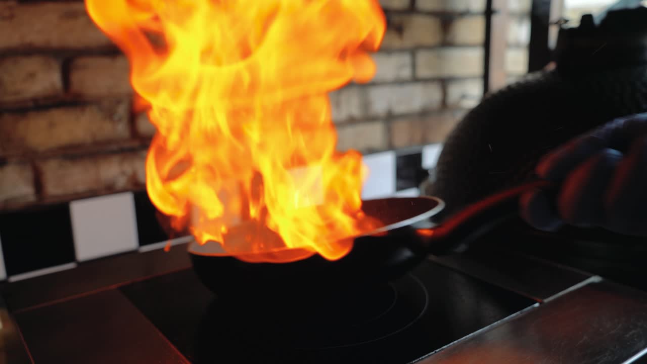 Chef sautes mushrooms with flames in restaurant while flipping around food. Professional cooking.