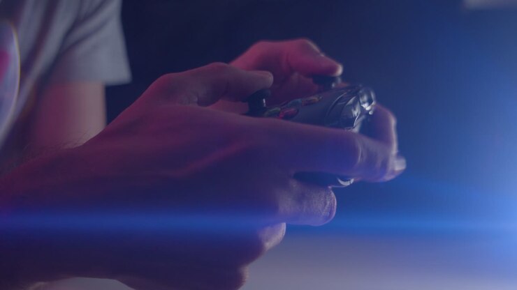 Giocare ai videogiochi in una stanza buia con un bagliore anamorfico dell'obiettivo sui pulsanti di un controller premuti rapidamente.