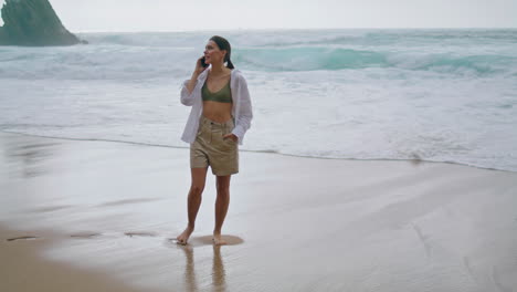 Gehende-Frau,-Die-Am-Bewölkten-Strand-Mit-Dem-Smartphone-Spricht.-Mädchen,-Das-Vertikal-Telefoniert