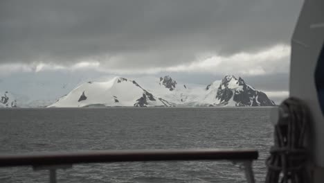 View-from-boat,-over-railing,-looking-to-mountain-on-coastline-covered-in-snow-and-ice