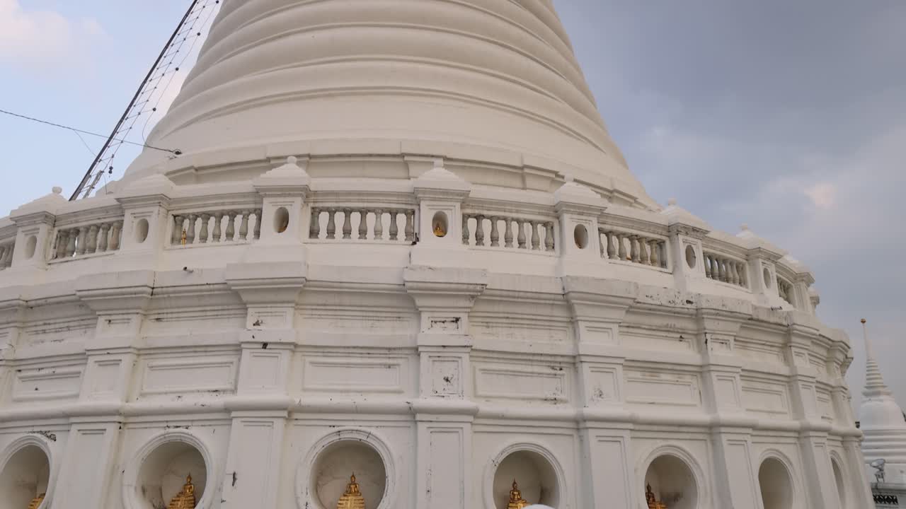 A serene view of the Prayurawongsawat Temple pagoda in Bangkok, showcasing its intricate architecture against a cloudy sky