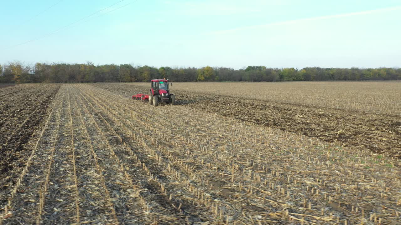 vista lateral aérea de un tractor que arrastra una harra de disco sobre un campo agrícola, tierras de cultivo