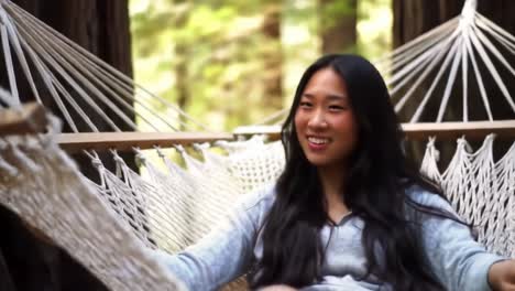 a joyful moment in nature: a young woman relaxing on a hammock amidst lush forest scenery, enjoying peace and tranquility in a serene outdoor setting