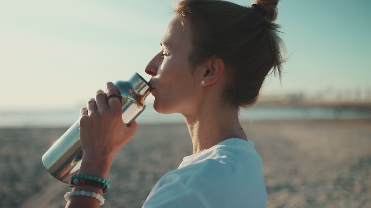 una deportista bebiendo agua en la playa.