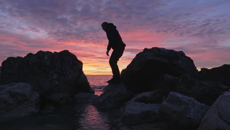 mans silhouette hops stone to stone during magical golden hour