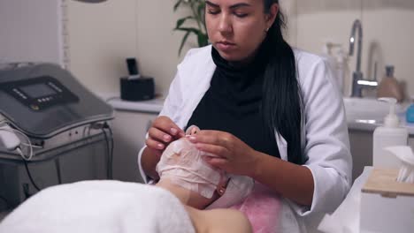 professional cosmetologist hands making face massage to the young woman with mask on her face and neck during cosmetic face