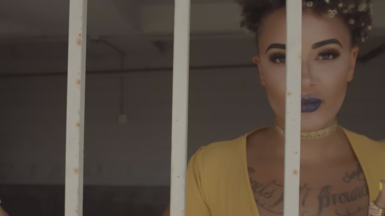 Young adult millennial woman blond afro dressed up in solar yellow dress full makeup and nails locked in a cell