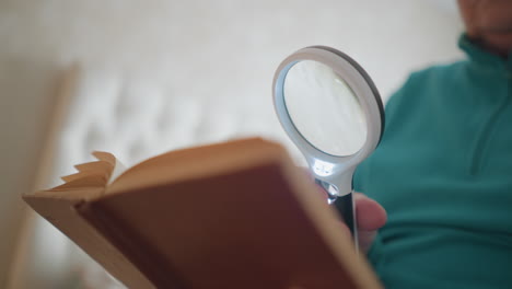 close-up view of elderly woman reading a book while holding a magnifying glass. her facial expression suggests focus and slight frustration as she examines the pages carefully