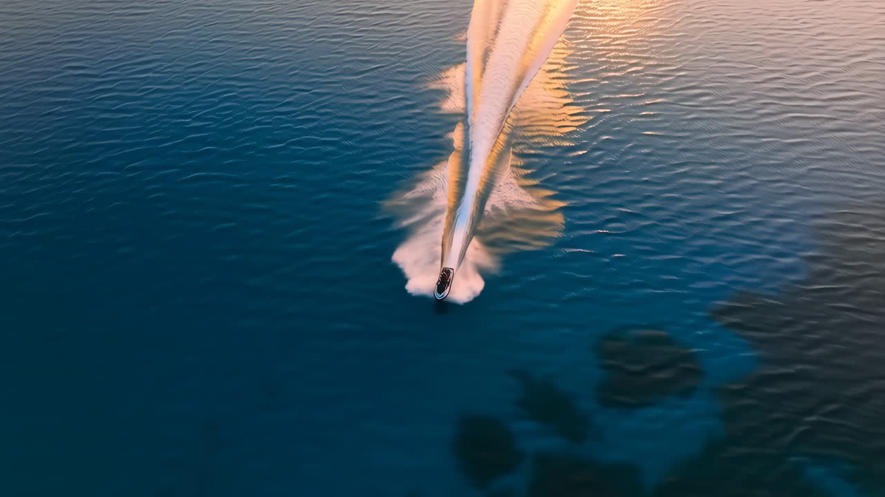 Aerial view of a speed boat leaving a wake on calm water at sunset