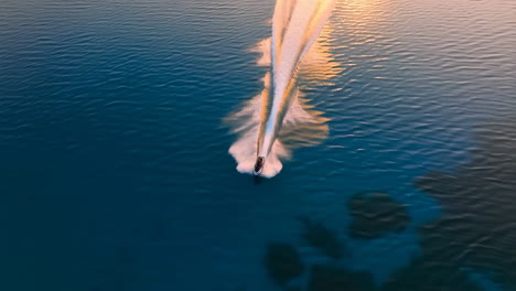 aerial view of a speed boat leaving a wake on calm water at sunset
