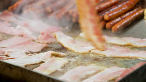 primer plano de voltear tocino con pinzas que se fríe en una sartén, preparación para el desayuno
