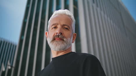 bearded man posing urban building closeup. confident senior male wear piercing