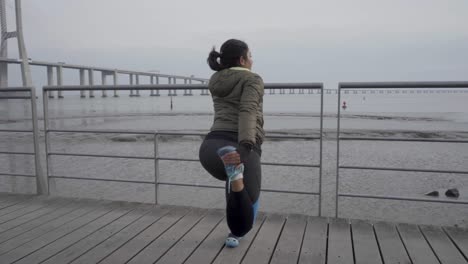 back view of young woman warming up before training on wooden pier