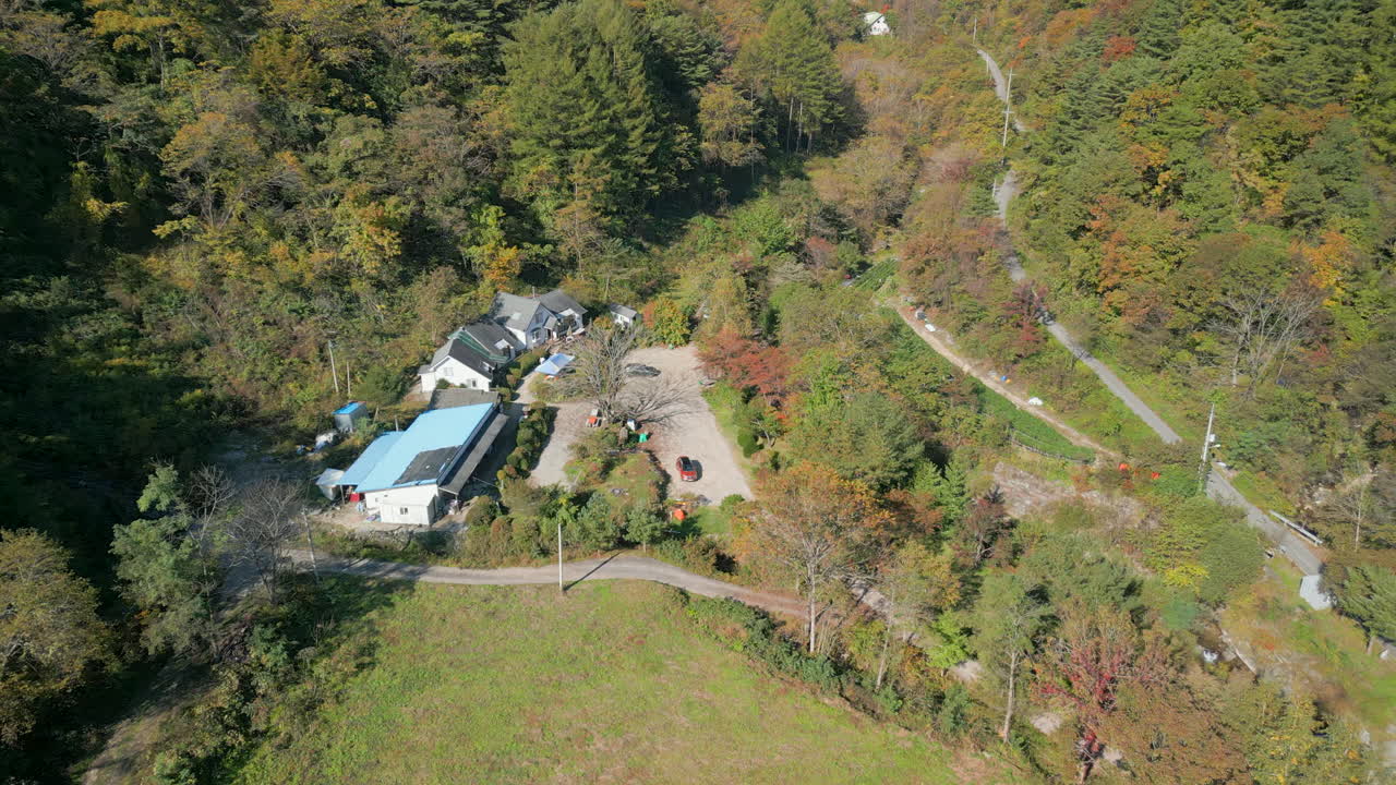 A steady shot moving towards a resthouse nestled among the dense, orange-hued autumn forest in the mountains
