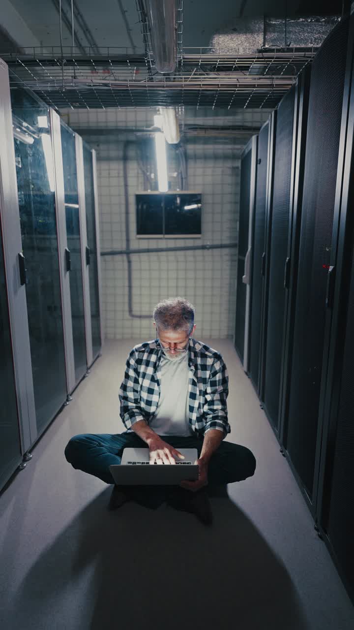 Man working on a laptop in a server room at night