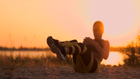 Joven-Y-Hermosa-Atleta-Practicando-En-La-Playa-Haciendo-Ejercicios-Para-Los-Músculos-De-Los-Abdominales-Al-Atardecer.-Girando-En-Cámara-Lenta