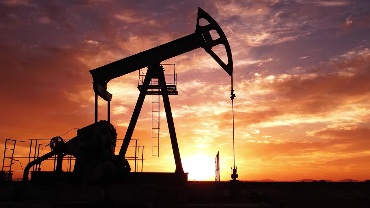 Silhouetted Oil Pump Jack Against a Stunning Sunset Sky: A Captivating View of Energy Extraction in the Turning Light of Day