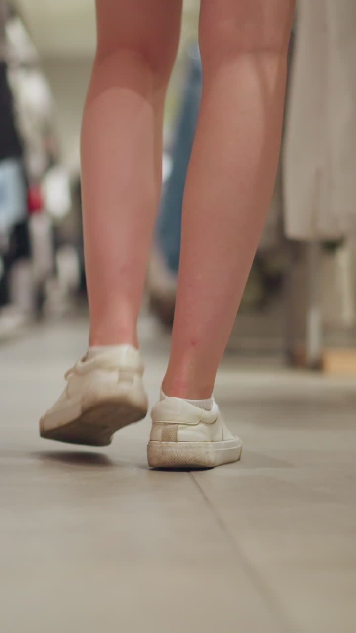 캔버스와 분홍색 쇼트를 입은 하 여자의 다리 시선, 그녀가 좌회전 할 때 옷 가게를 통해 조용히 고, 옷은 끔하게 그룹으로 배열되어 있으며, 배경은 밝습니다.