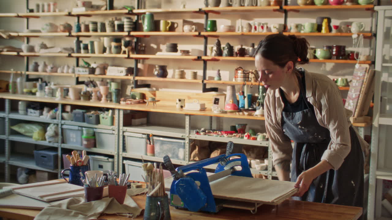 Female Artisan Flattening Clay with Roller Machine in Pottery Studio