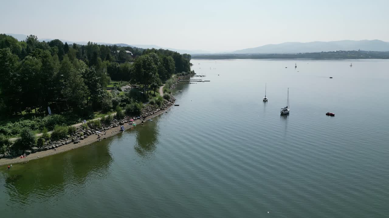 orilla de un lago sereno en las montañas beskid, rodeada de vegetación durante un día de verano - vista aérea 4k