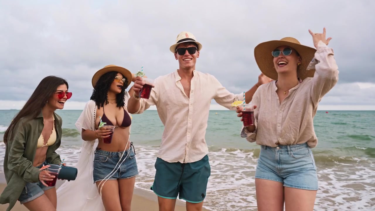 Giovani amici felici che ballano e festeggiano con drink sulla spiaggia