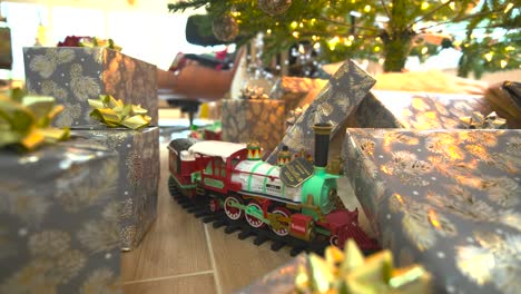 captivating stock footage: glide beneath a festive christmas tree, presents galore, showcasing a model train, spreading joy in a delightful wide reverse sliding shot