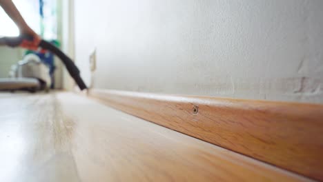 man cleaning off the dust on a baseboard with a vacuum cleaner