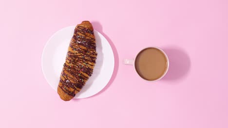 fresh delicious chocolate croissant rotating with cup of coffee on pastel pink background. stop motion