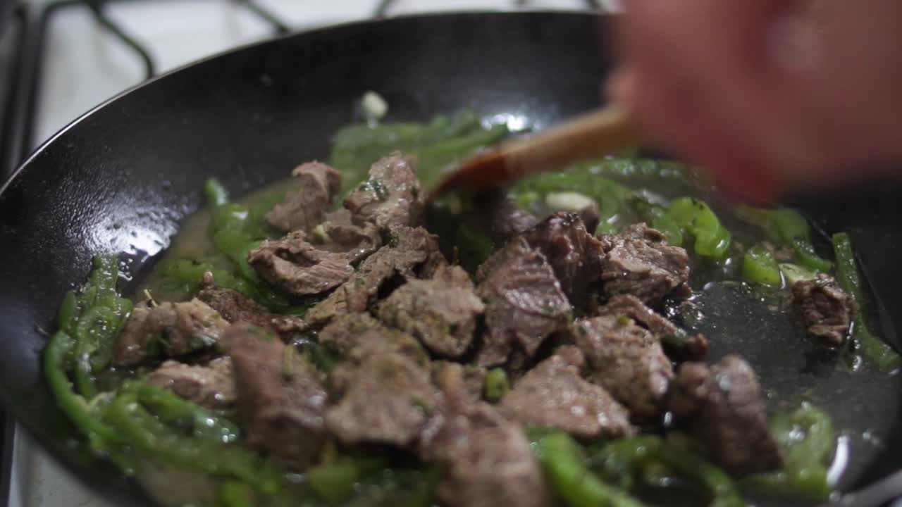 Jarak dekat wajan berasap berisi daging dan paprika hijau yang baru dibuka, diaduk dengan sendok kayu