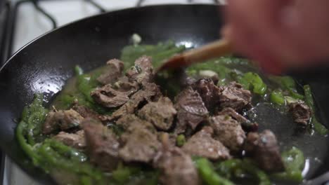 closeup uncovering smoking pan with meat and green pepper, stiring with wooden spoon