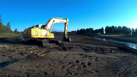 yellow excavator works with bucket to clear mud sludge and debris from the bottom of the drained river-1