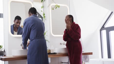 African-american-couple-talking-and-using-face-cream-in-bathroom-in-the-morning,-slow-motion