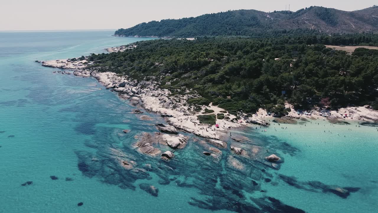 Rising drone shot of Beach Kavourotrypes at Chalkidiki island ,Greece during sunny day - greened mountains in Background with clear ocean water