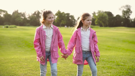 two happy little sisters in identical clothes holding hands and walking together in the park