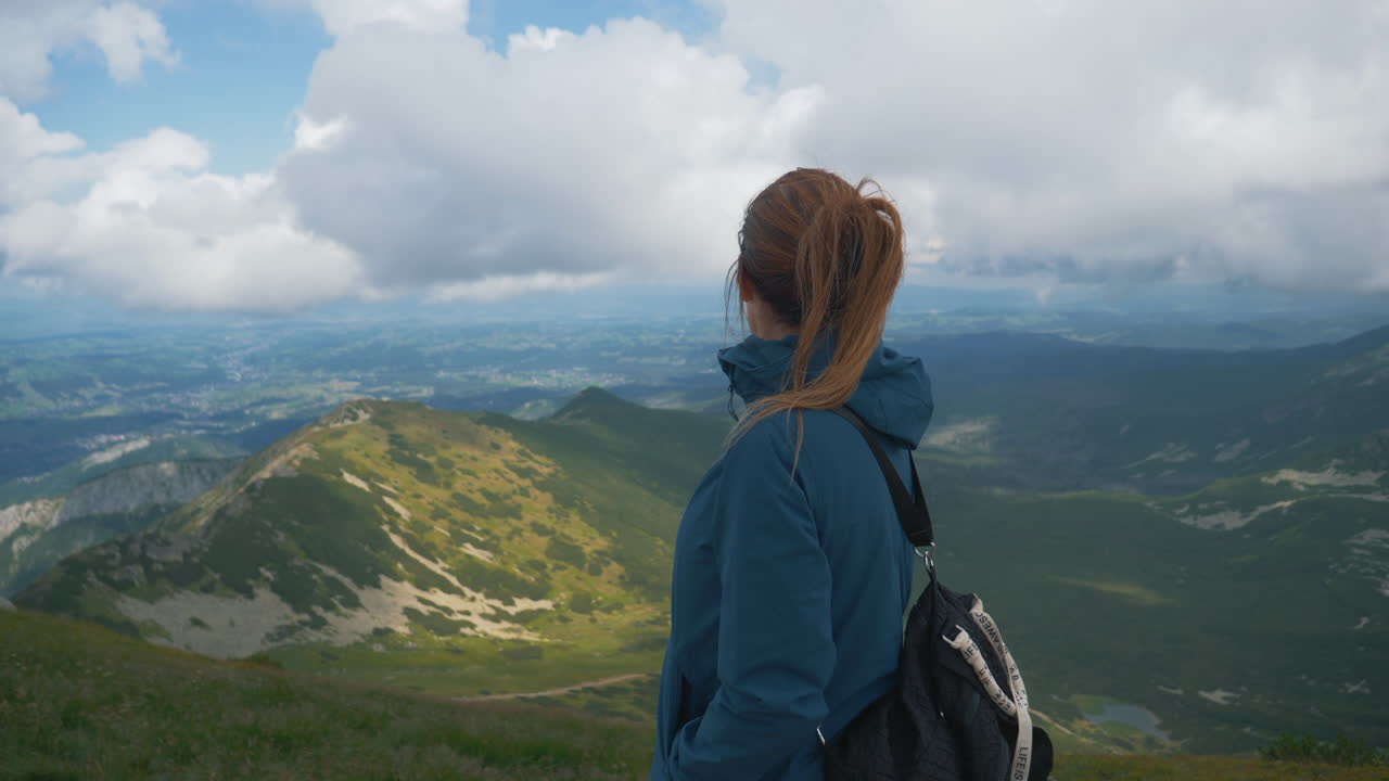 female traveler with a backpack looking at a beautiful mountain landscape from the summit
