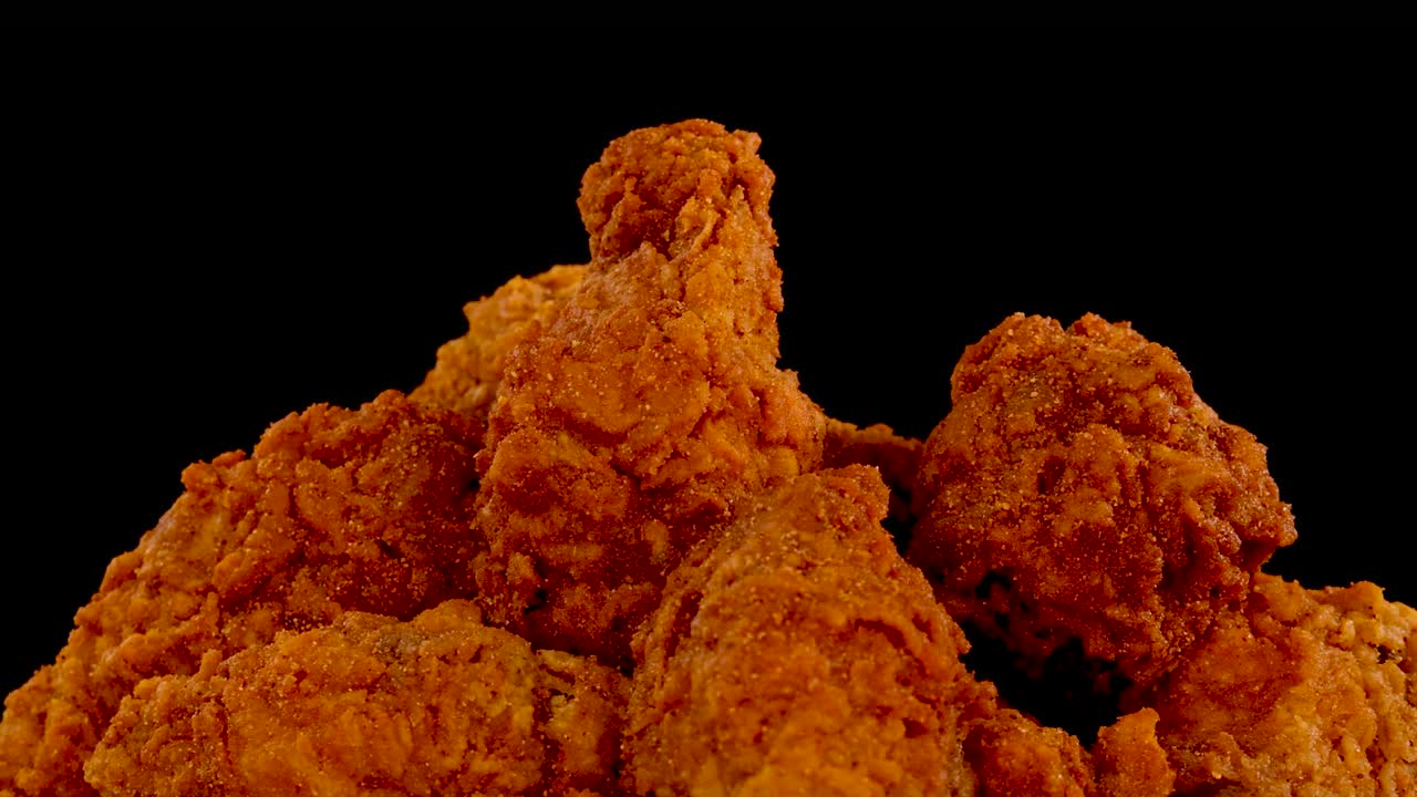 Crispy, golden-brown fried chicken pieces are shown in extreme close-up against a black background, with a slow zoom-in effect and dramatic lighting