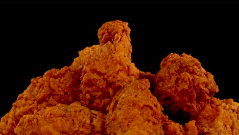 crispy, golden-brown fried chicken pieces are shown in extreme close-up against a black background, with a slow zoom-in effect and dramatic lighting