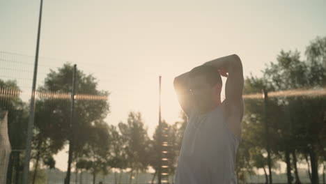 concentrated sportsman doing tricep stretch exercises in outdoor court at sunset 1